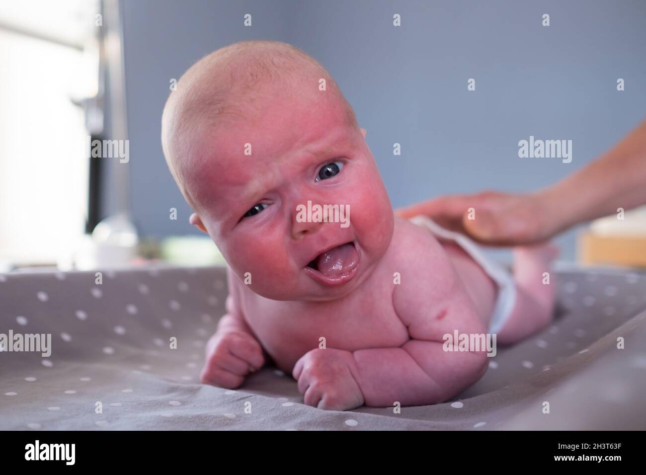 baby girl crying at camera being upset as it is difficult for her to lay on belly Stock Photo