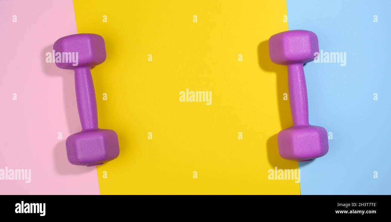 Two purple plastic kilogram dumbbells on a bright colored background, top view. Stock Photo