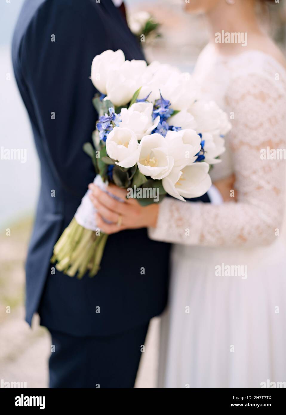 The bride and groom stand hugging and hold a wedding bouquet with white and blue flowers and eucalyptus branches close-up Stock Photo