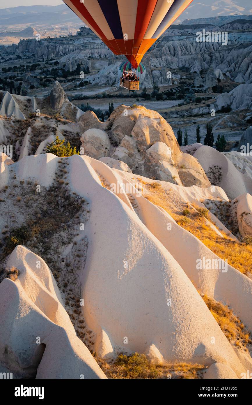 GOREME, TURKEY - AUGUST 3, 2021: Close up of colorful hot air balloons with basket full of tourists flying very close to the ground over the Cappadoci Stock Photo