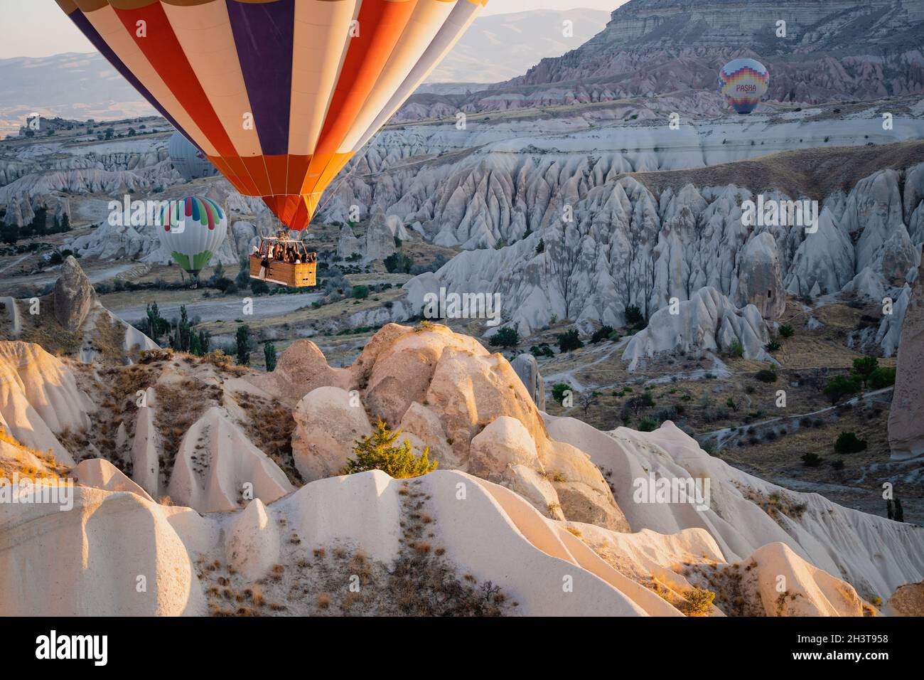 GOREME, TURKEY - AUGUST 3, 2021: Close up of colorful hot air balloons with basket full of tourists flying very close to the ground over the Cappadoci Stock Photo