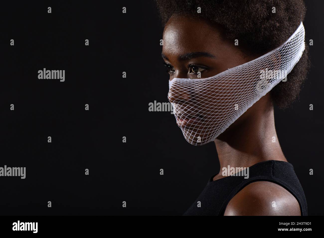 Closeup portrait of african american woman fashion model wearing quarantine medical face mask coarse mesh net on black backgroun Stock Photo