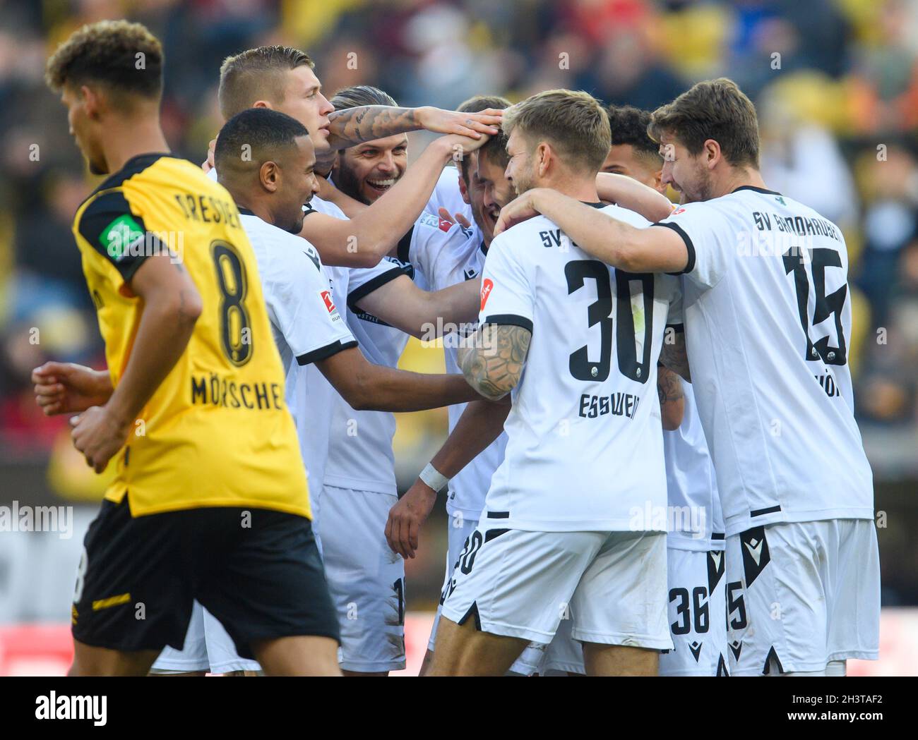 30 October 2021, Saxony, Dresden: Football: 2. Bundesliga, SG Dynamo Dresden - SV Sandhausen, Matchday 12, at Rudolf-Harbig-Stadion. Sandhausen's Pascal Testroet is cheered by his teammates after scoring the 0:1 goal while Dynamo's Heinz Mörschel (l) runs past. Photo: Robert Michael/dpa-Zentralbild/dpa - IMPORTANT NOTE: In accordance with the regulations of the DFL Deutsche Fußball Liga and/or the DFB Deutscher Fußball-Bund, it is prohibited to use or have used photographs taken in the stadium and/or of the match in the form of sequence pictures and/or video-like photo series. Stock Photo