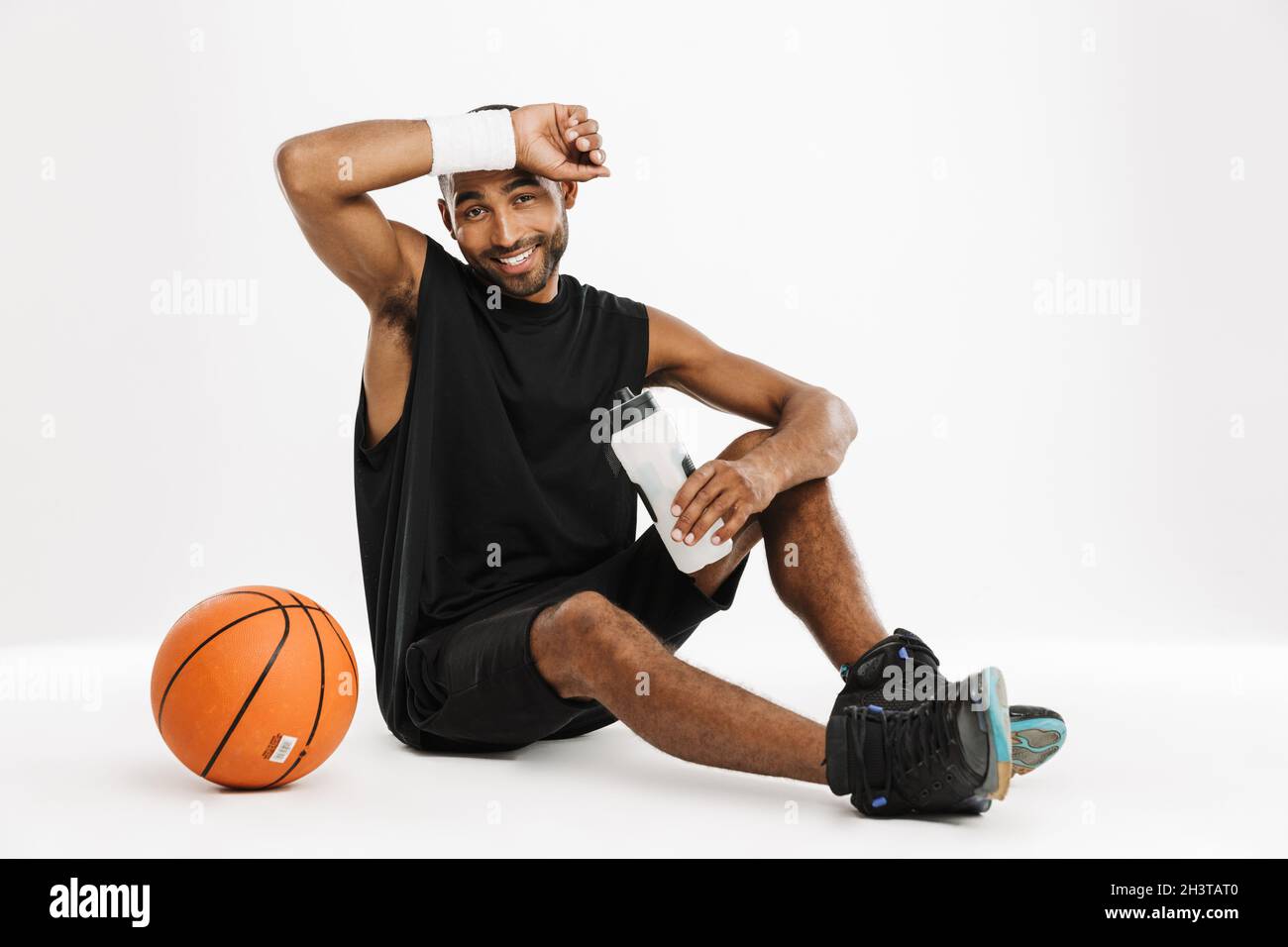 Happy african young basketball player sitting reasting holding bottle of water isolated on a white background Stock Photo