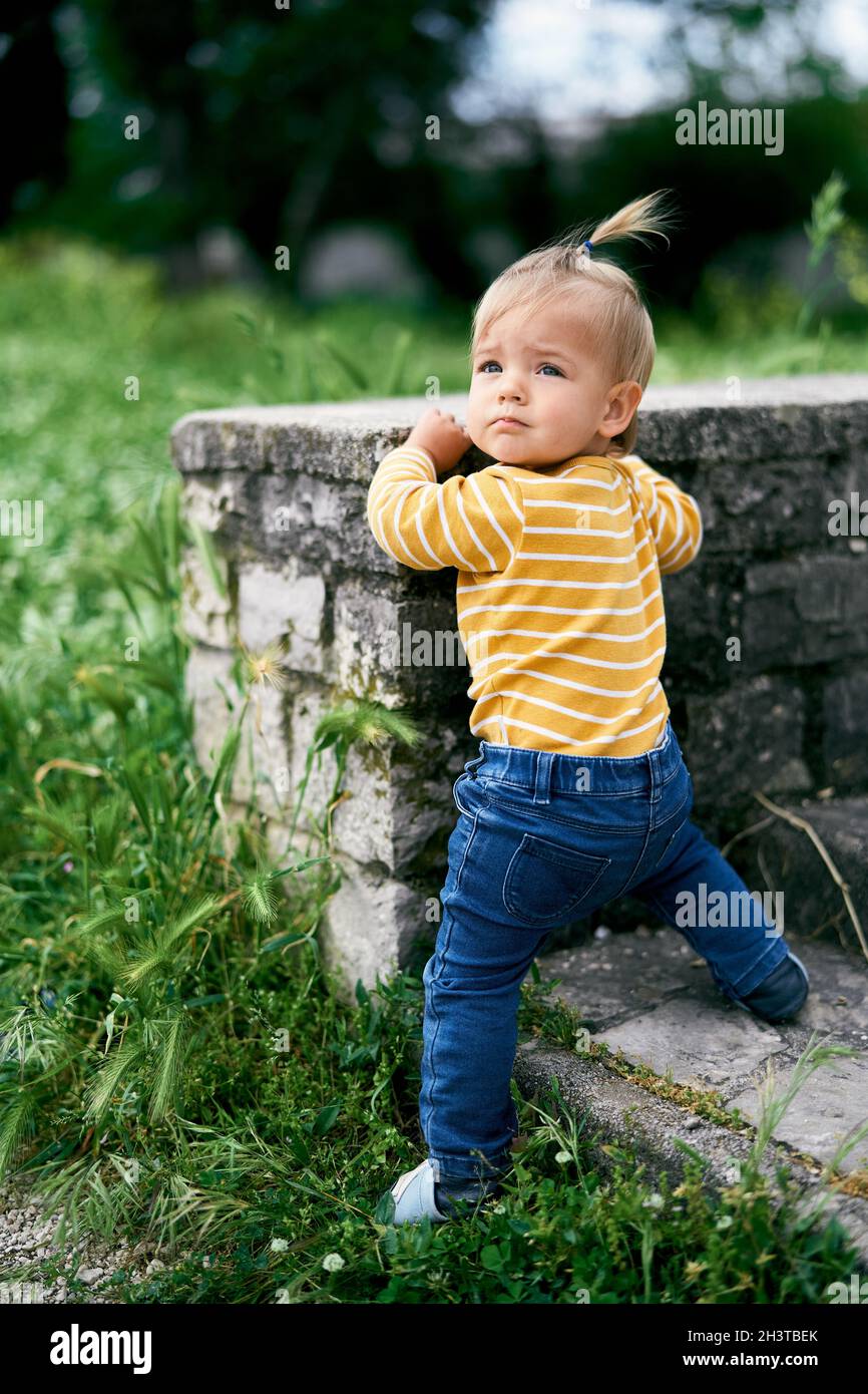 Little girl stands at a stone fence in the park, turning her head Stock Photo
