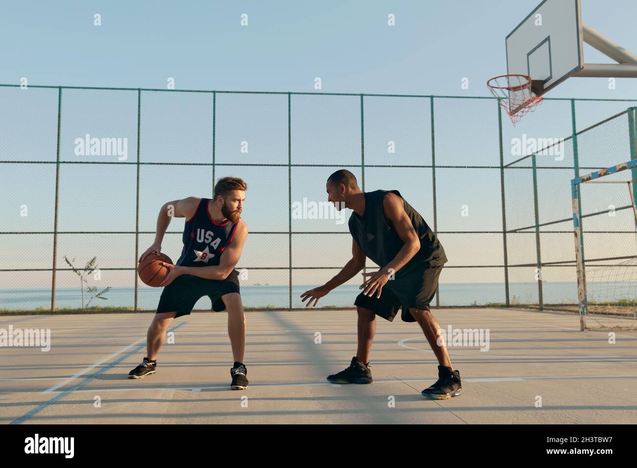 Young athletic men playing basketball on sports court. Black and