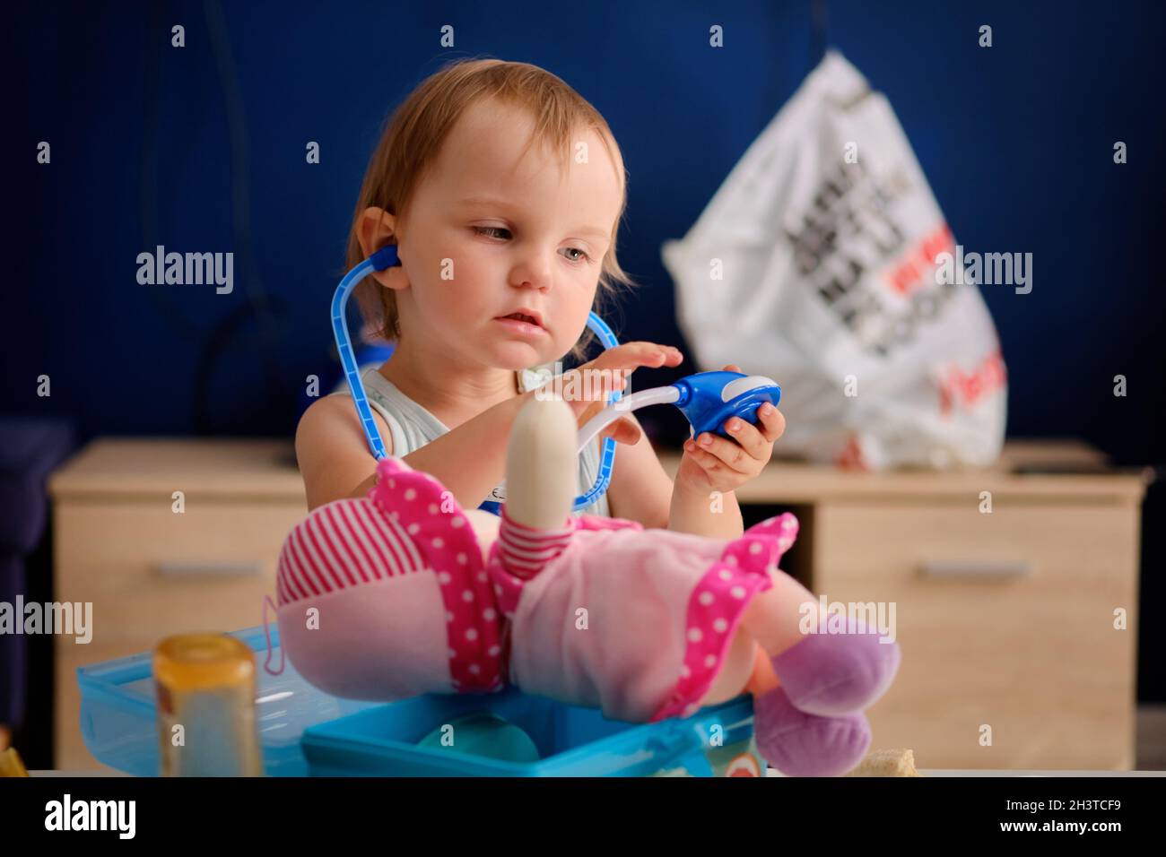 cute little blond girl is playing doctor with her pink rag doll Stock Photo