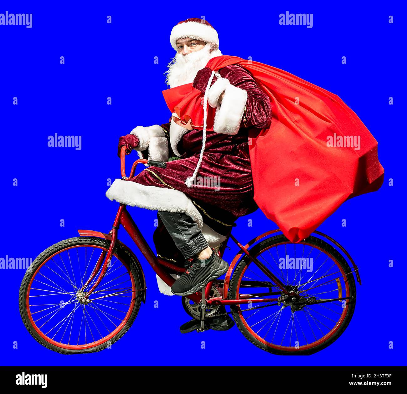 Cheerful Santa Claus in a New Year's hat and red suit clothes rides a  bicycle with a bag of gifts. Isolate. Happy new year 2022. Happy Christmas.  Conc Stock Photo - Alamy