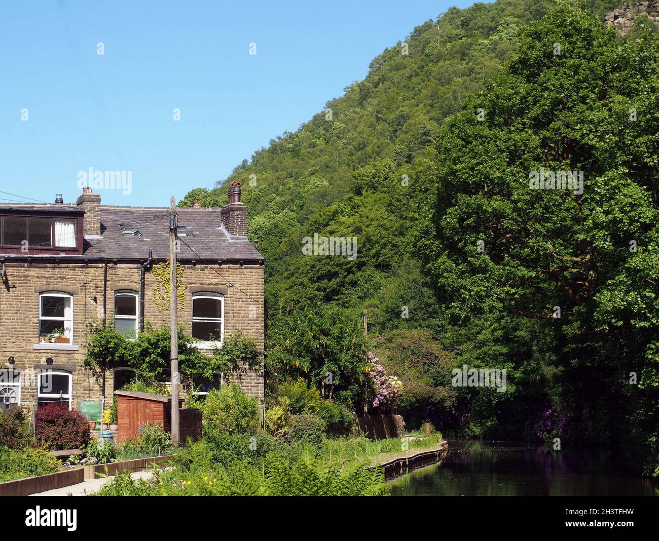 A canal path surrounded by summer flowers with a row of old stone houses at eastwood in hebden bridge west yorkshire Stock Photo