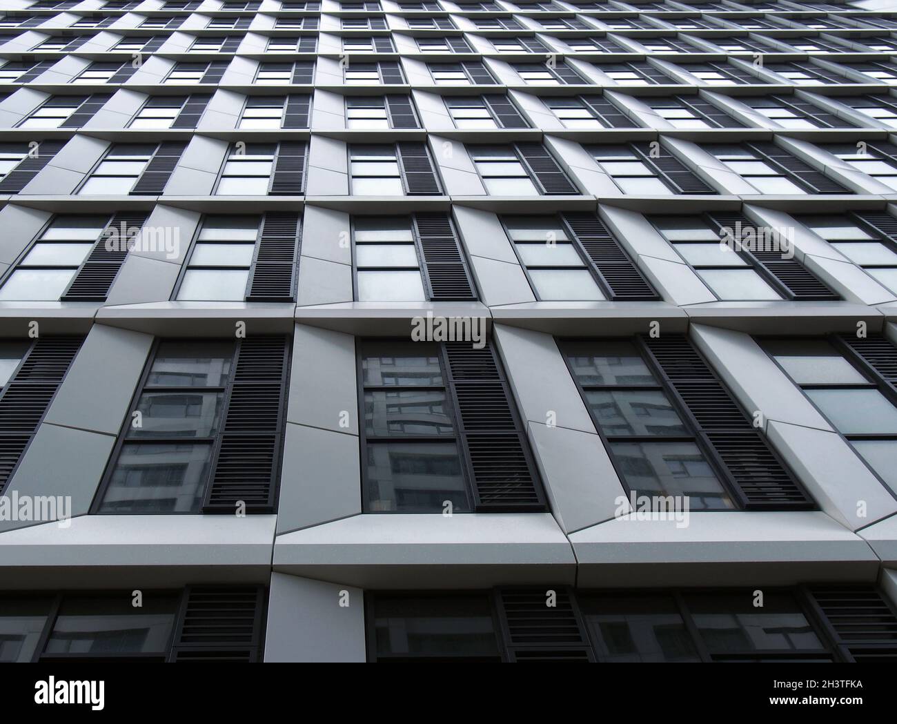 Close up perspective detail of tall high rise modern apartment building with geometric white cladding and dark windows Stock Photo