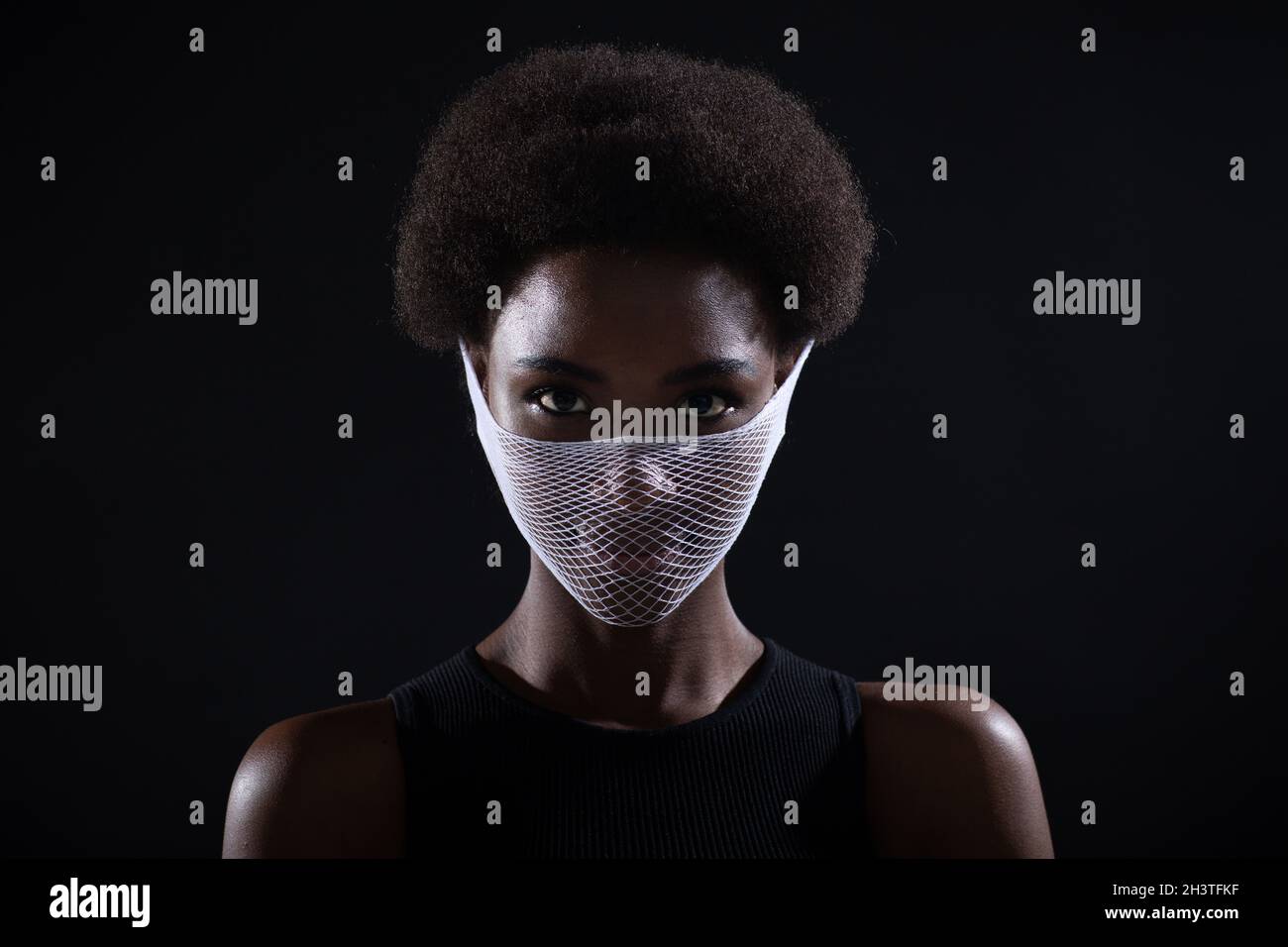 Closeup portrait of african american woman fashion model wearing quarantine medical face mask coarse mesh net on black backgroun Stock Photo