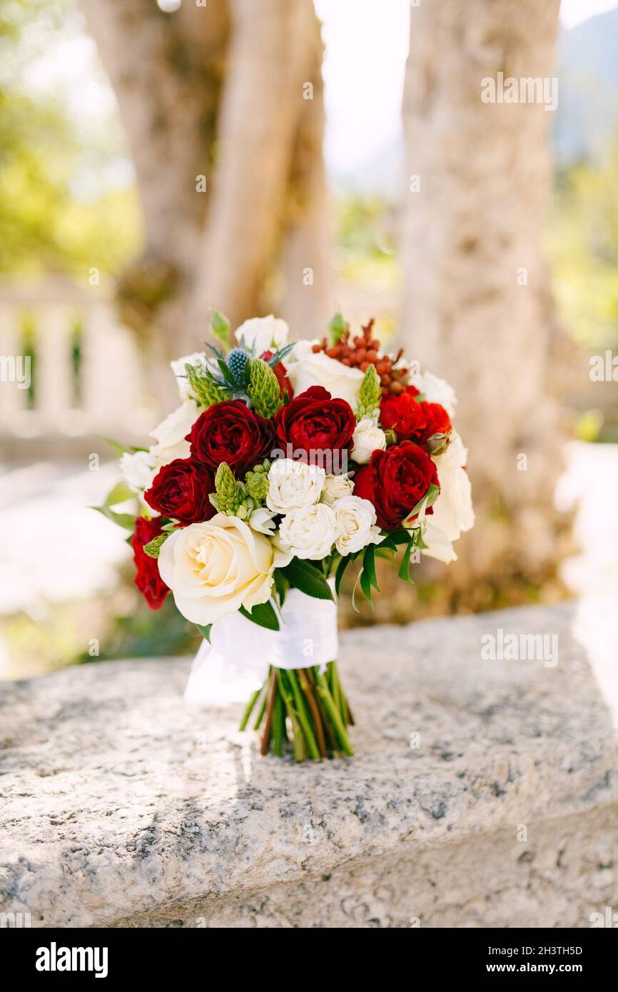 Bridal bouquet of white, read and cream roses, ornithogalum, eryngium with white ribbons on the fence Stock Photo
