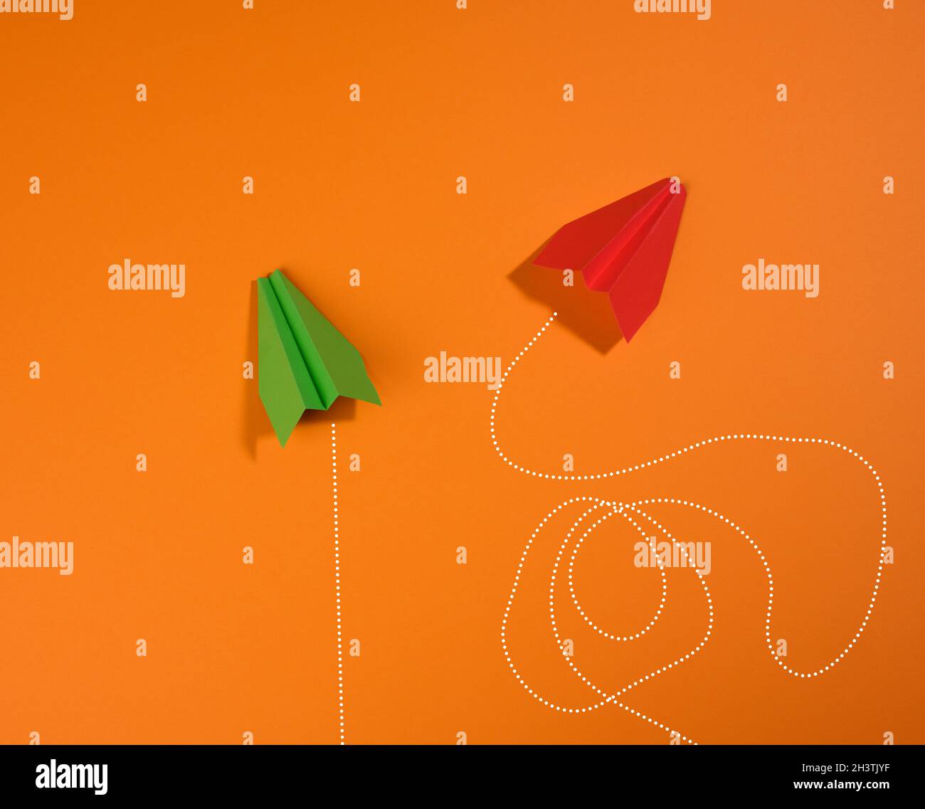 Two paper airplanes with different trajectory of movement on an orange background Stock Photo