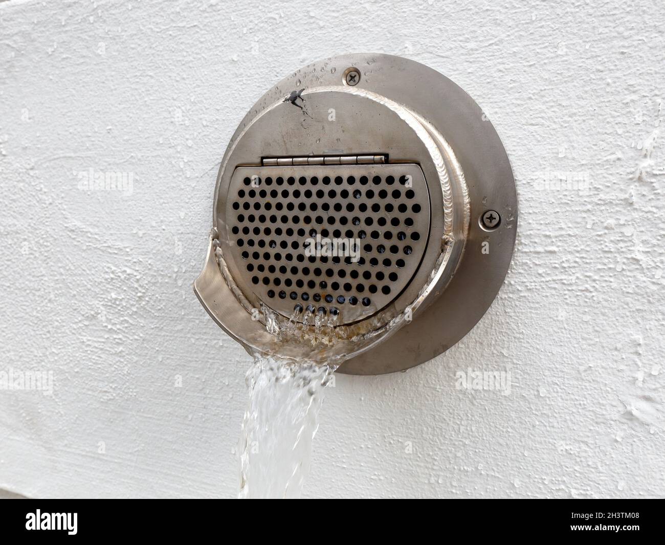 Water pouring from a downspout nozzle on the side of a building during a rain storm. Stock Photo