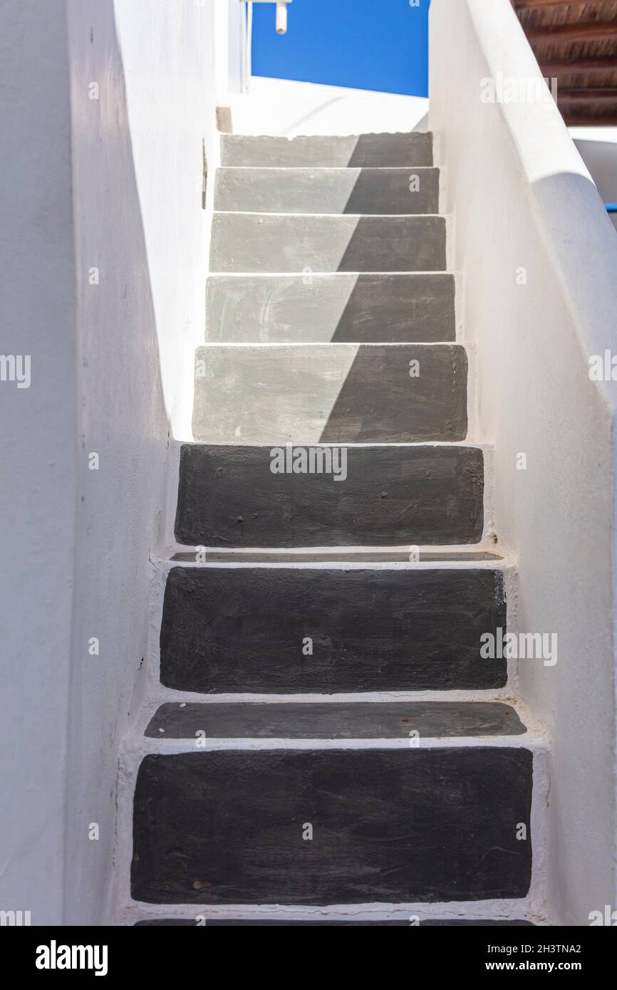 Exterior stone stairs grey empty narrow half sunny between whitewashed building walls drives to Greek blue sky. Kythnos island Cyclades Greece. Under Stock Photo