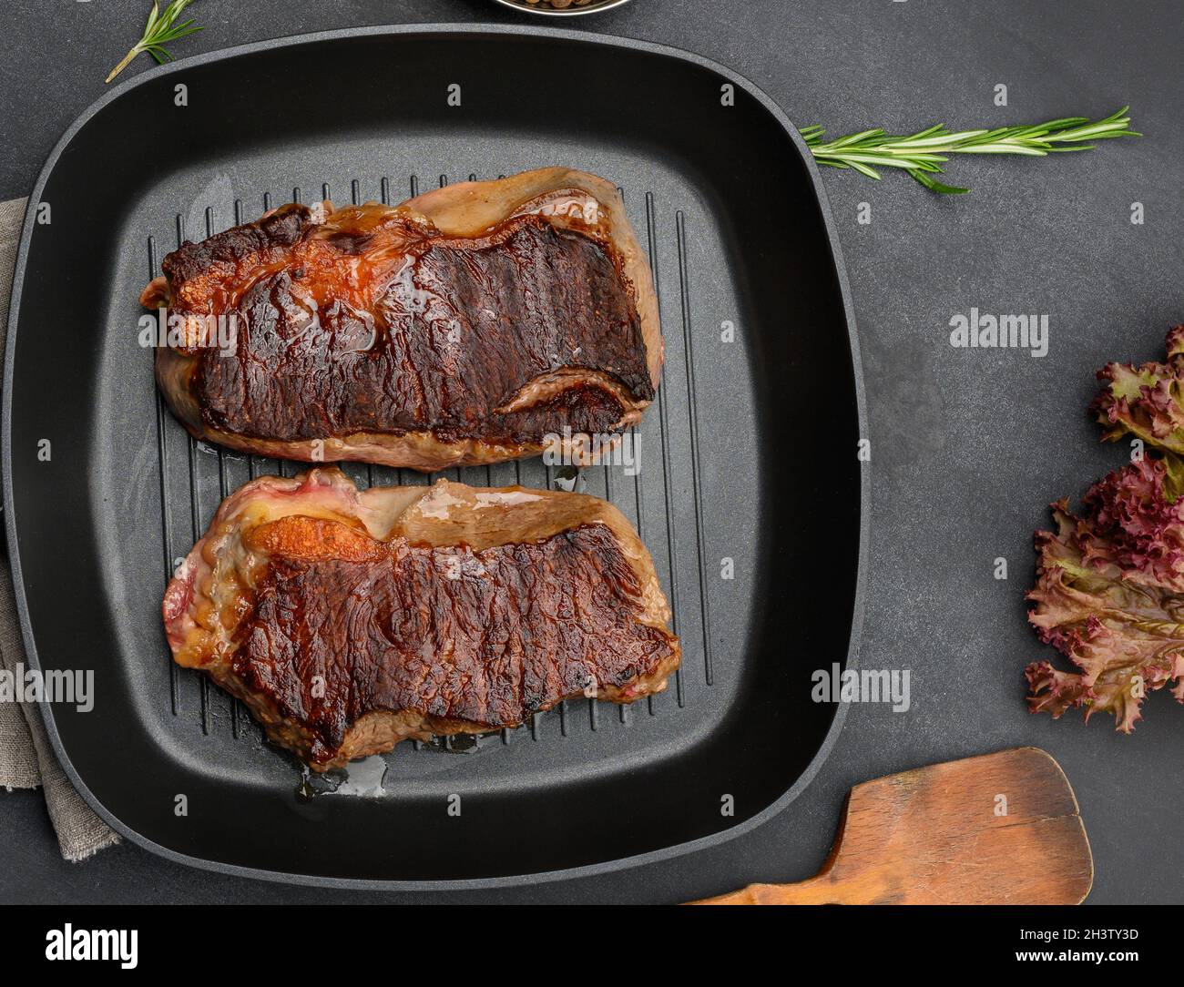 Two fried beef pieces are in a frying pan on a black table, degree of readiness of the dish is well don Stock Photo