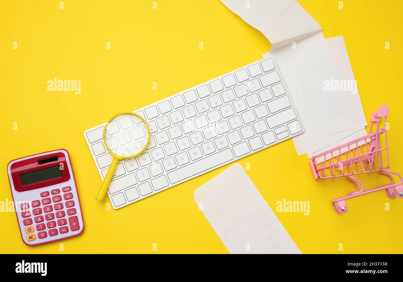 White wireless keyboard, stack of paper receipts and magnifier on yellow background, budget analysis concept Stock Photo