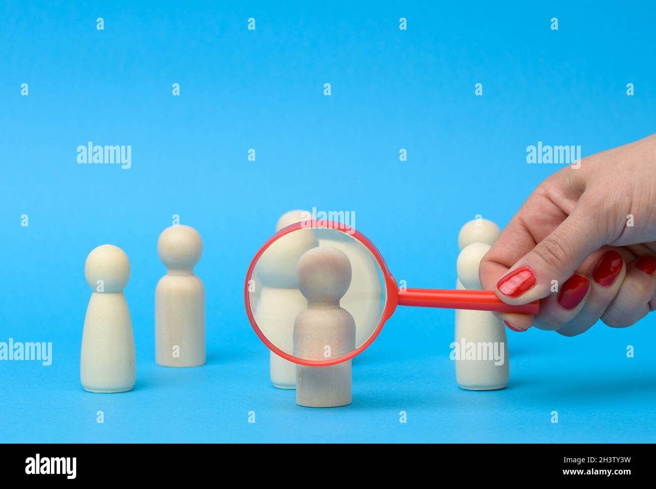 Wooden figures of men stand on a blue background and a red magnifying glass Stock Photo