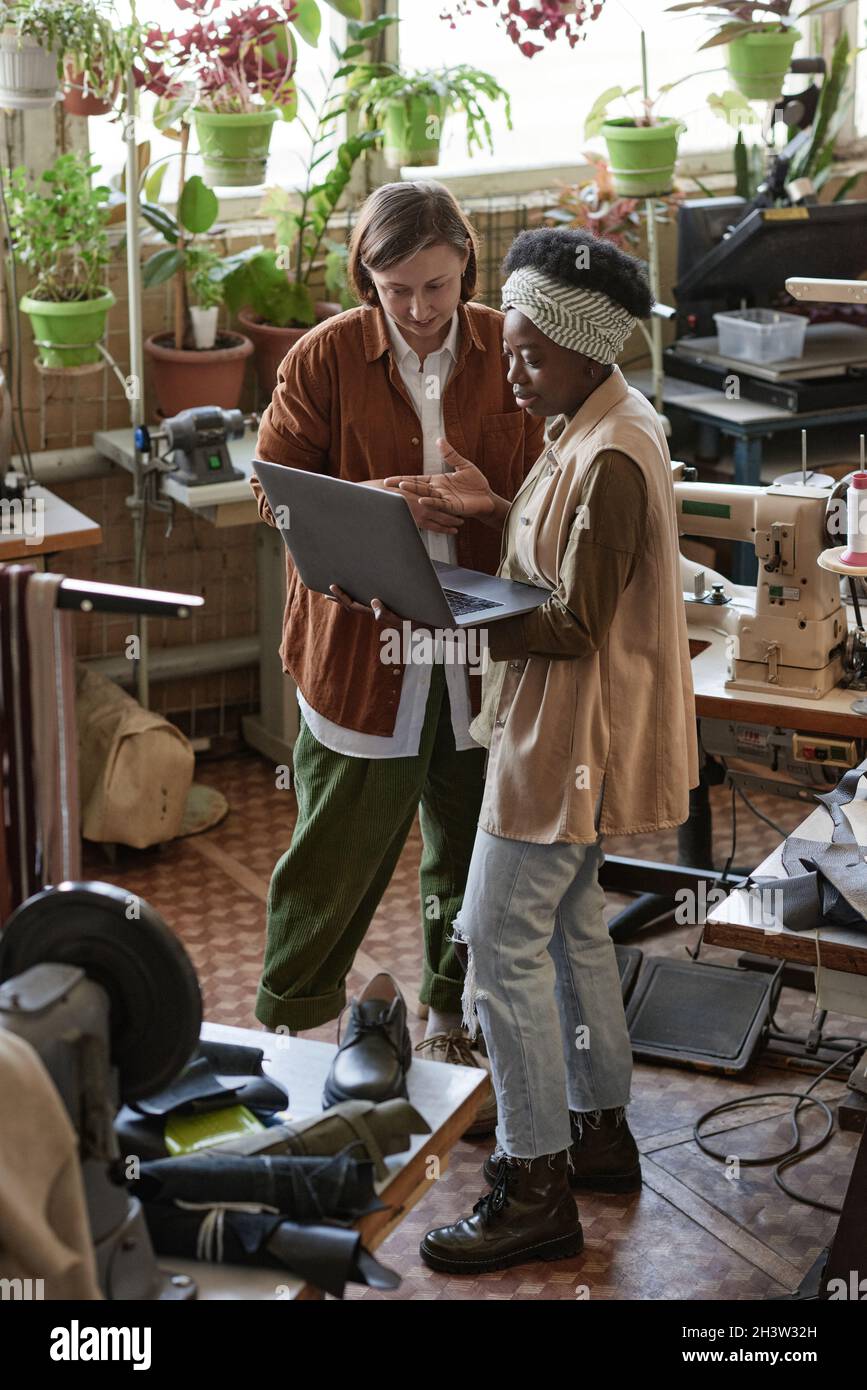 African designer discussing clothes collection with businessman using laptop while they standing in the workshop Stock Photo