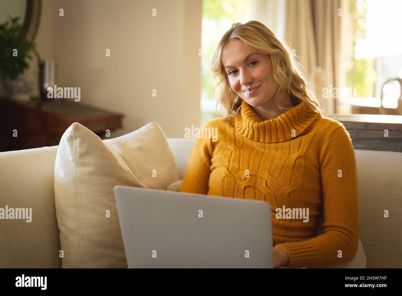 Portrait of happy caucasian woman sitting on couch in living room using ...