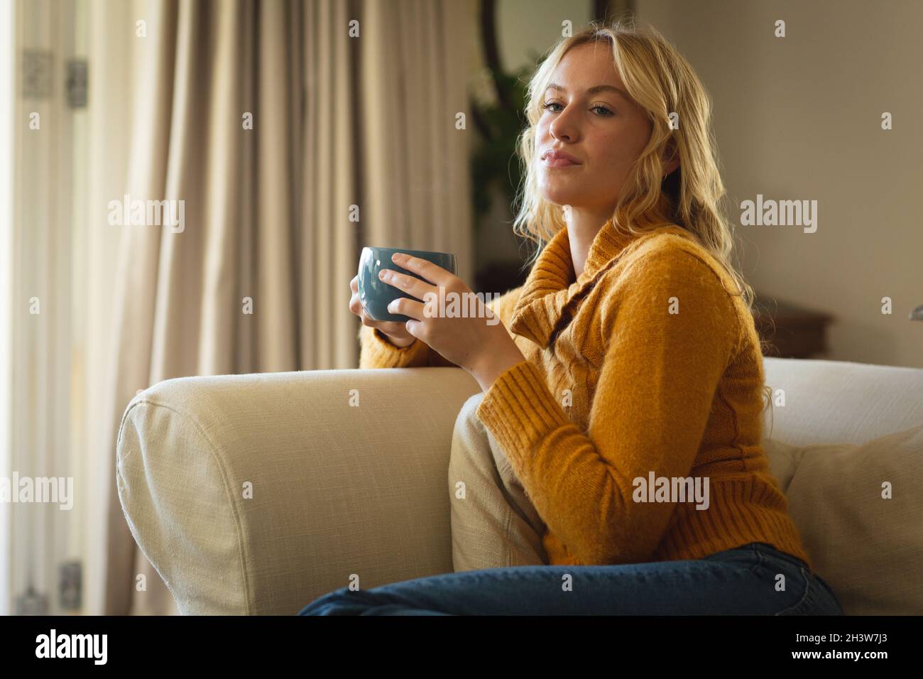 Thoughtful caucasian woman sitting on couch in living room holding ...