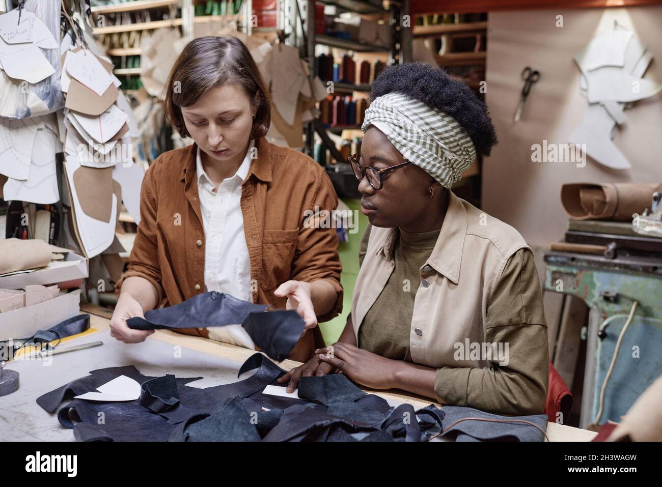 Two tailors sitting at their workplaces and sewing pieces of the fabric in team during their work in the workshop Stock Photo