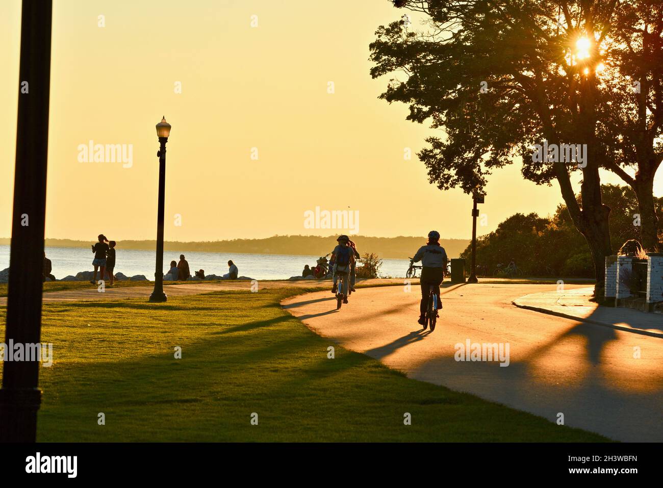 People gathering to watch golden sunset and bicyclists biking on road