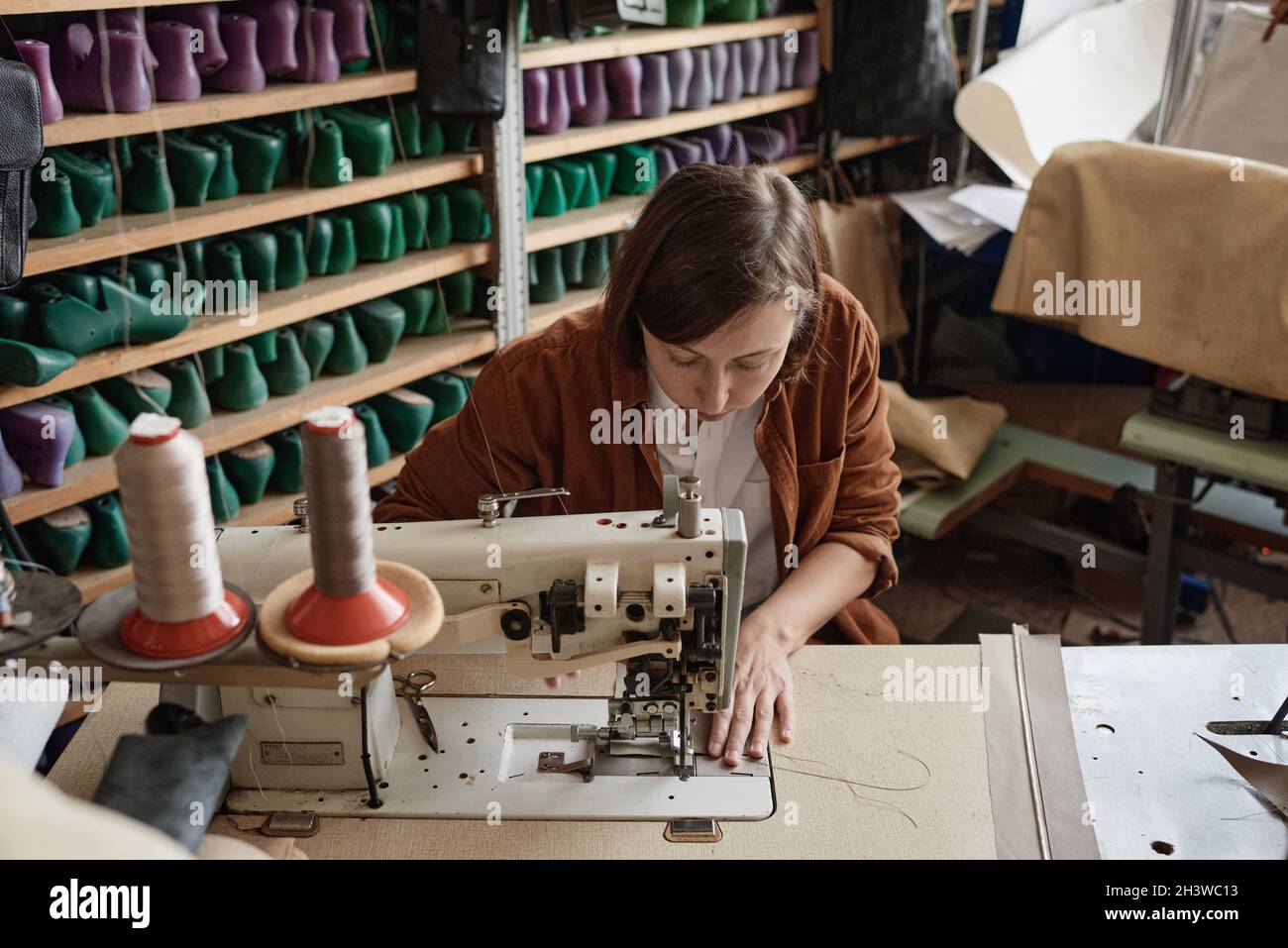 Shoemaker sitting at the table and using sewing machine in her work