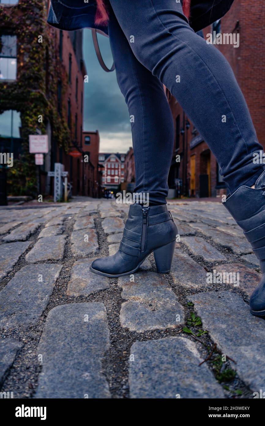 A women wearing jeans and black boots walks down a cobblestone street Stock  Photo - Alamy