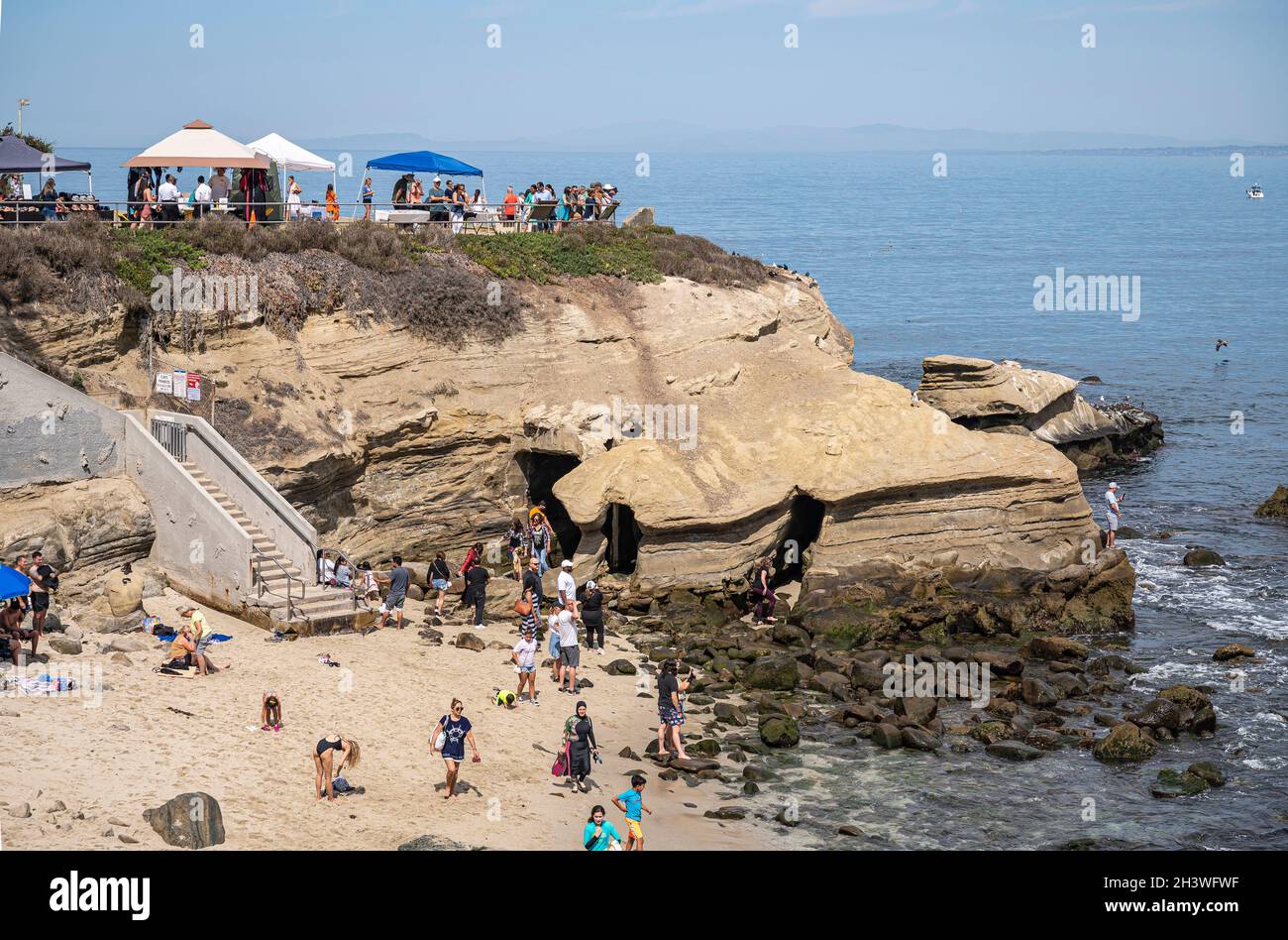 La Jolla, California, USA - October 3, 2021: La Jolly cove beach with dark caves in beige stone rocky cliffs at ocean water with plenty of people arou Stock Photo
