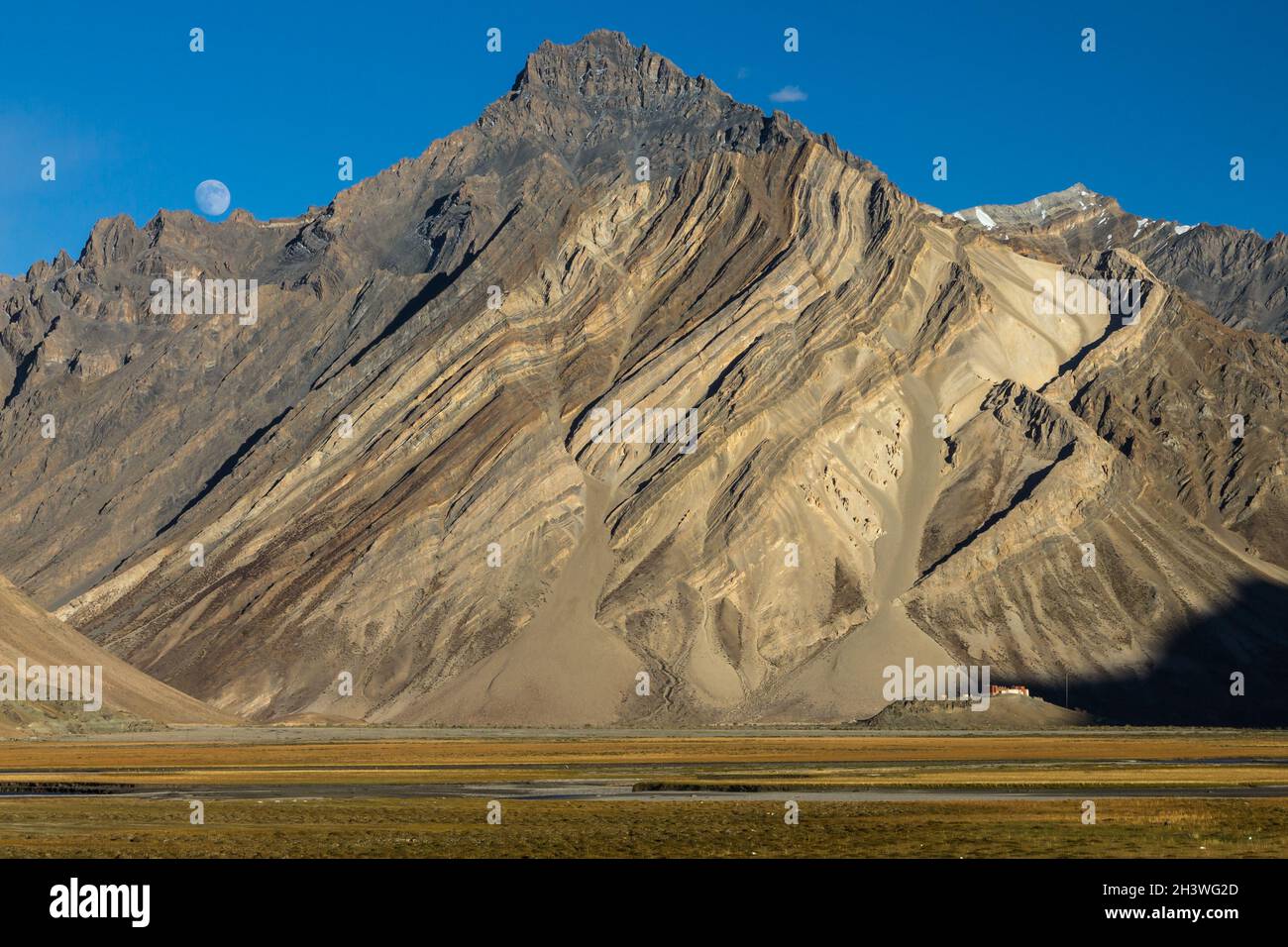 Zanskar Mountains cliff with clearly visible sediment rock layers, Rangdum Gompa and the rising moon Stock Photo