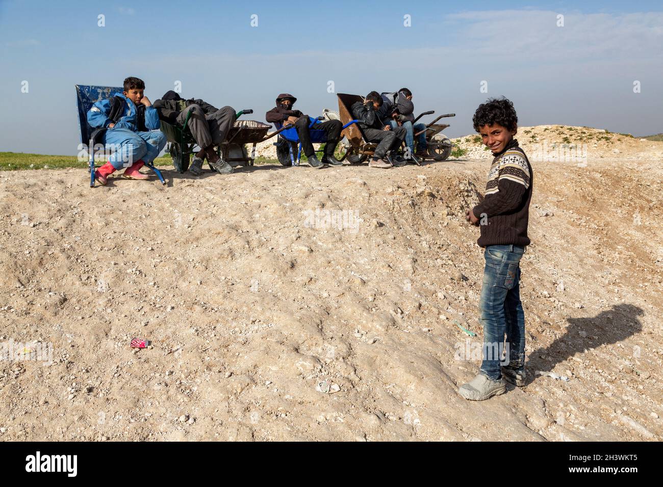 Syrian children carrying the belongings of Syrian refugees in a wheelbarrow for money. Stock Photo