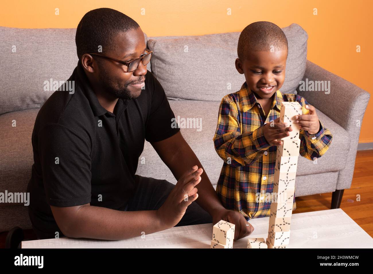 Preschool age boy at home building with wooden puzzle blocks, father encouraging him Stock Photo