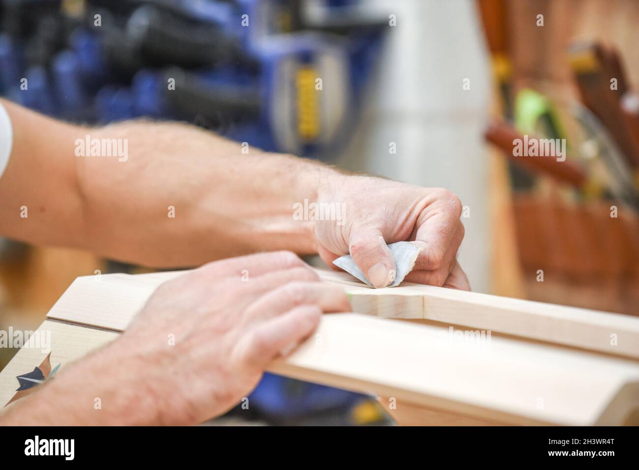 The man is sanding wood with sand paper in part of the furniture making