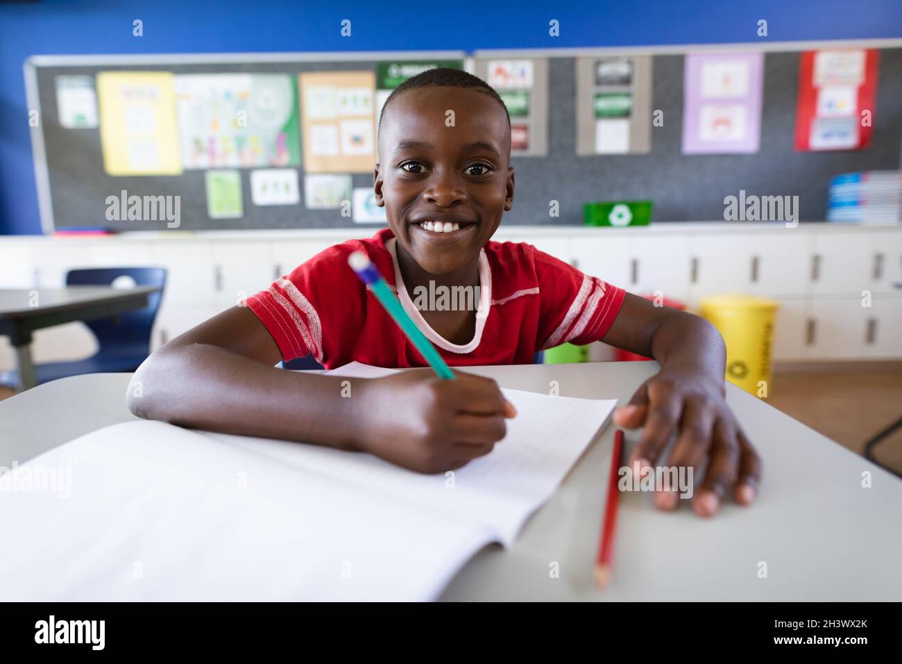 Portrait of african american boy smiling while sitting on his desk in ...