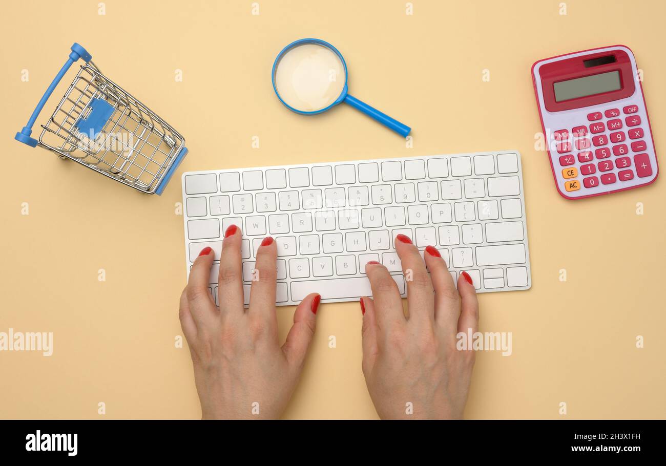 Female hands and white wireless keyboard, stack of paper receipts and magnifier on yellow background Stock Photo