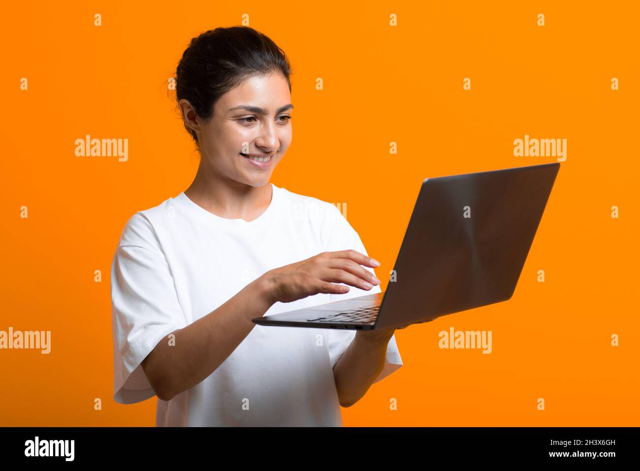 Portrait of young smiling adult indian woman working with laptop computer. Stock Photo