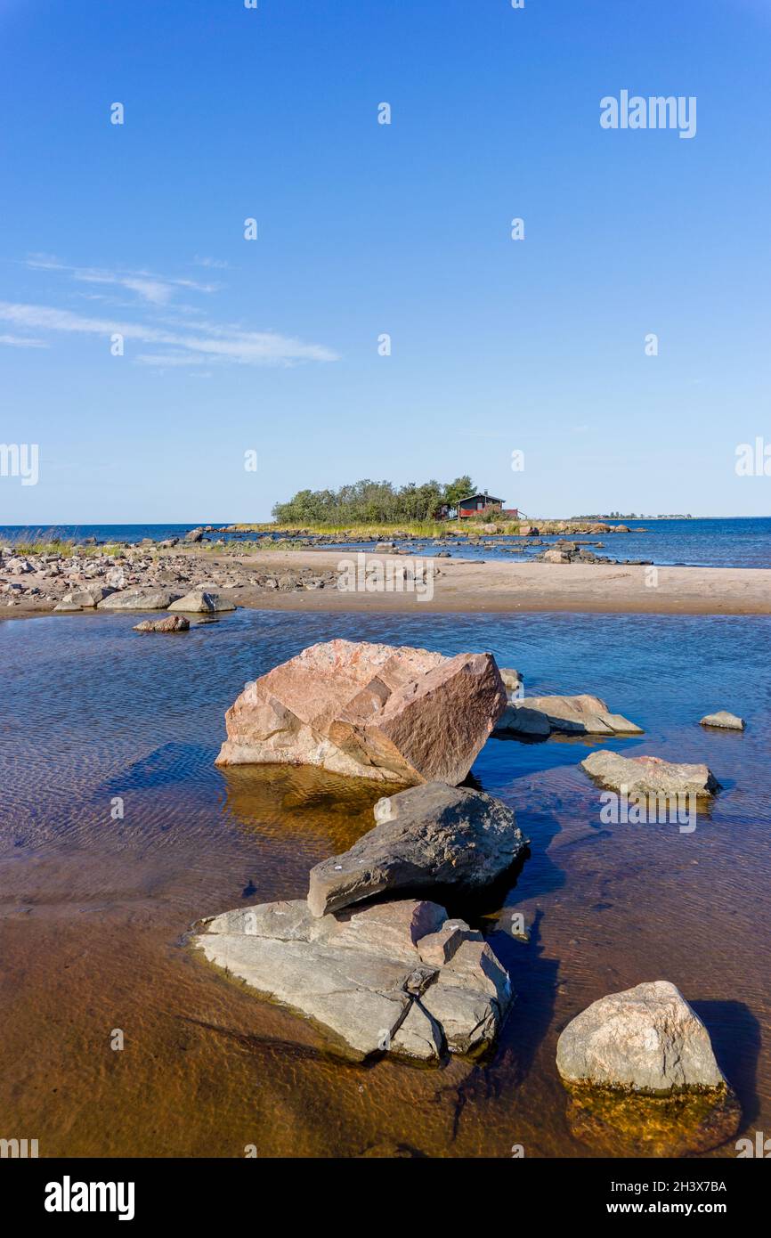 Picturesque coastal landscape on the Baltic Sea with a small red cottage on an island behind a sandy beach under a blue sky Stock Photo