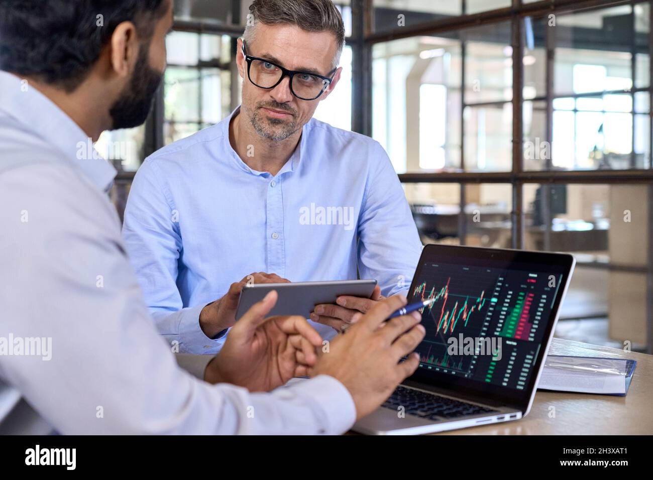 Diverse businessmen traders discussing cryptocurrency at desk using devices. Stock Photo