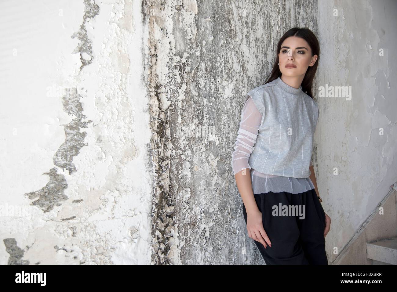 Young woman wearing grey tshirt and black trousers standing in an abandond factory and looking away. Stock Photo