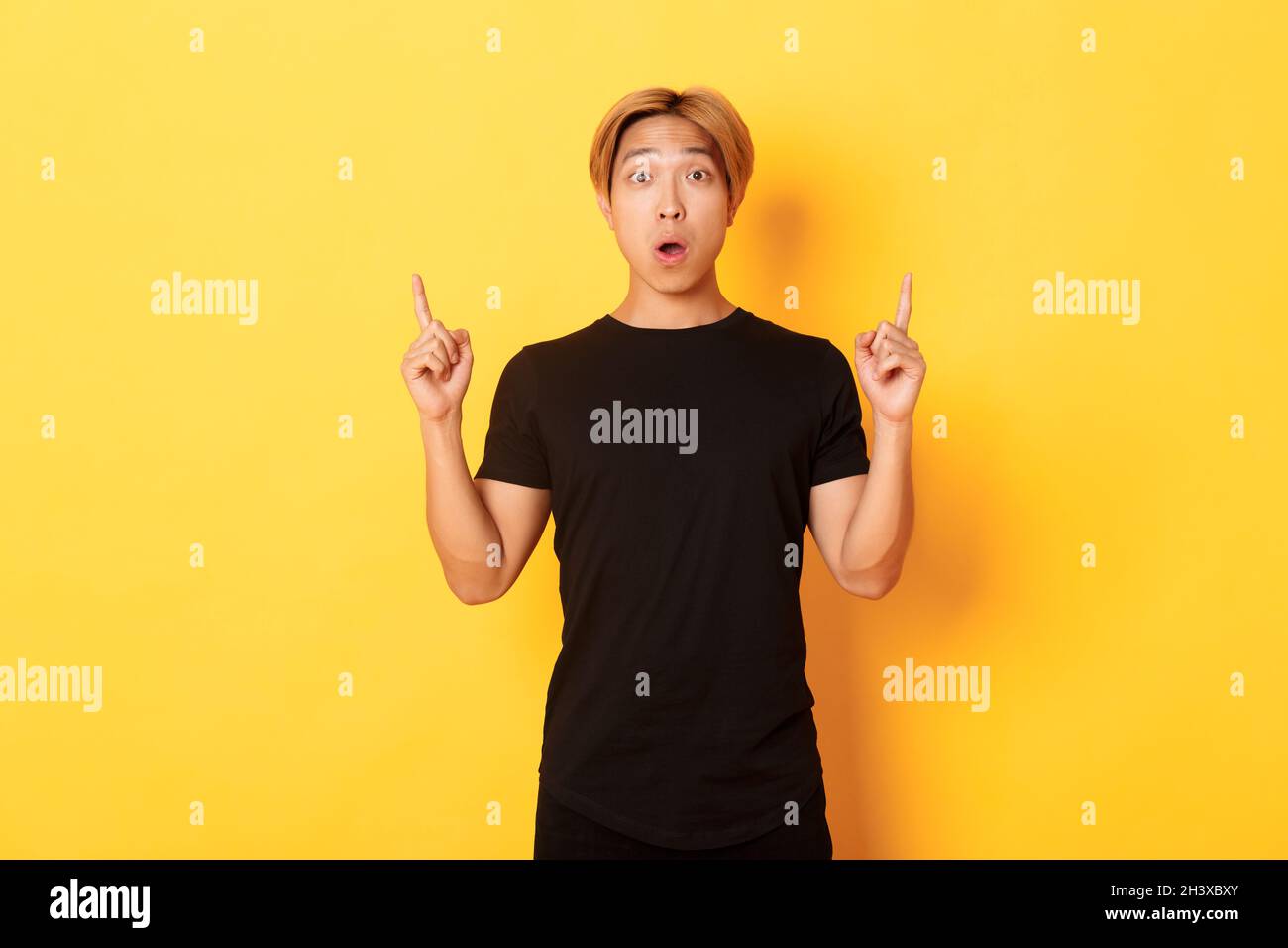 Portrait Of Astonished Asian Guy In Black T Shirt Open Mouth Fascinated Pointing Fingers Up