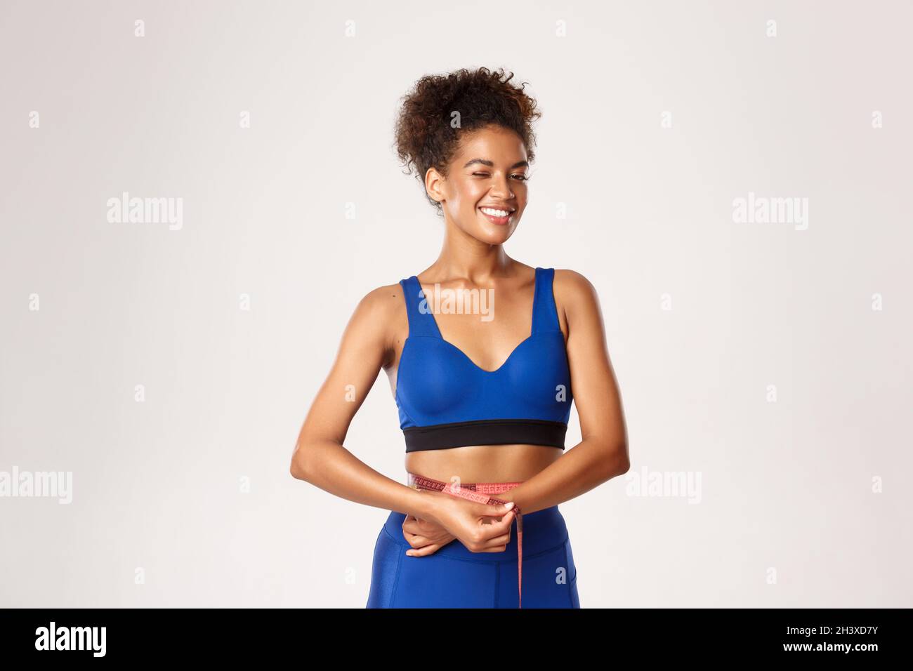 Attractive african-american fit female athlete losing weight, measuring  waist with tape and winking satisfied at camera, white b Stock Photo - Alamy