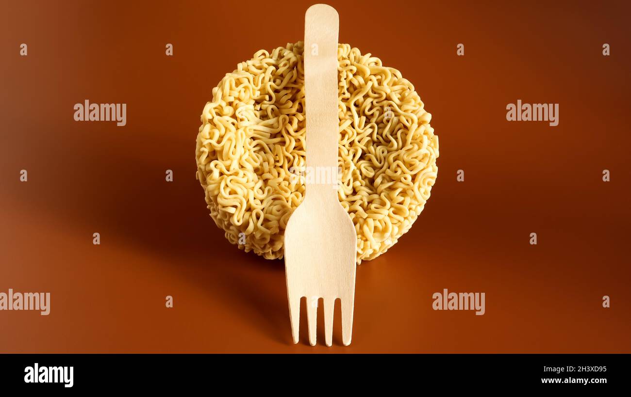 Raw instant noodles in the shape of a circle with a wooden disposable fork. pasta, for the preparation of which it is enough to Stock Photo