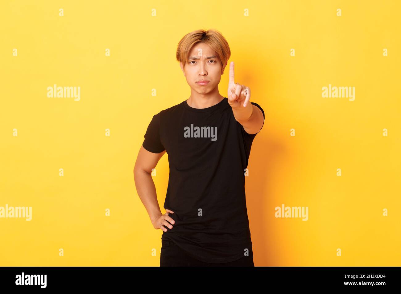 Portrait of serious-looking disappointed asian man shaking finger to scold someone, standing yellow background Stock Photo