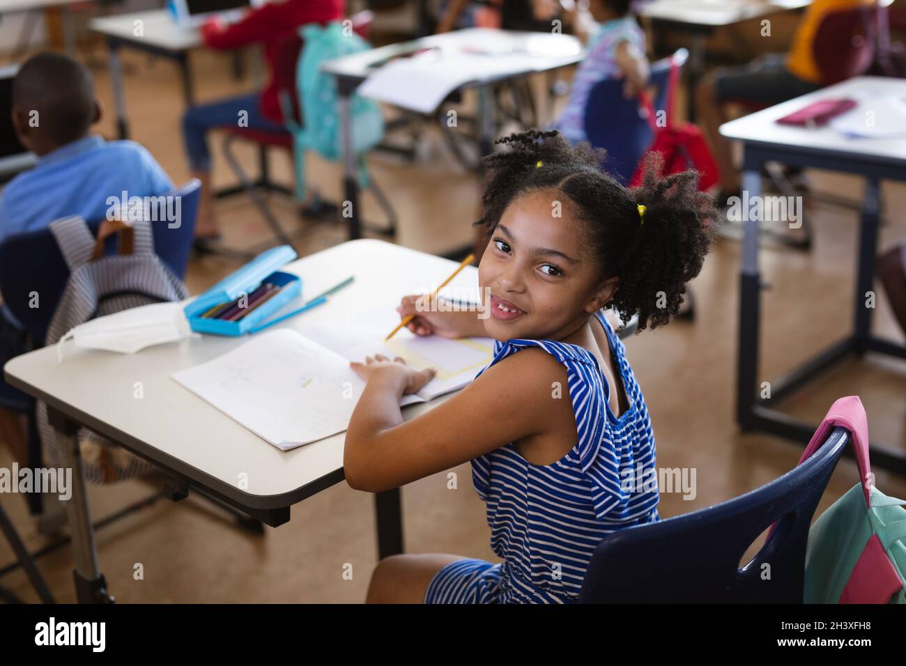 Portrait of african american girl smiling while sitting on her desk in ...