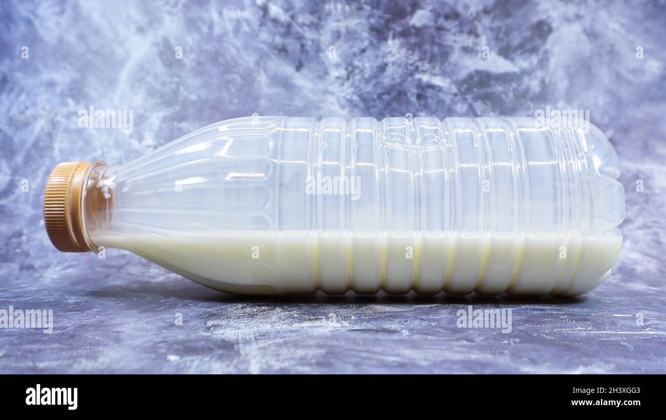 A semi-empty plastic bottle of fresh regular milk lies on a dark gray marble or concrete backdrop. Close-up front view. World mi Stock Photo