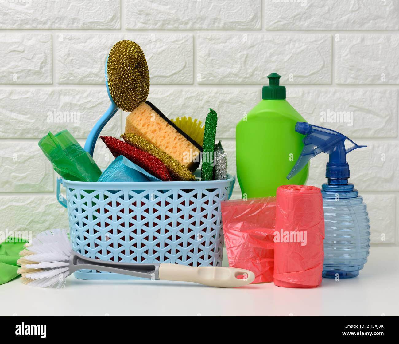 Plastic basket with brushes, disinfectant in a bottle, rubber gloves on the background of a white brick wall Stock Photo