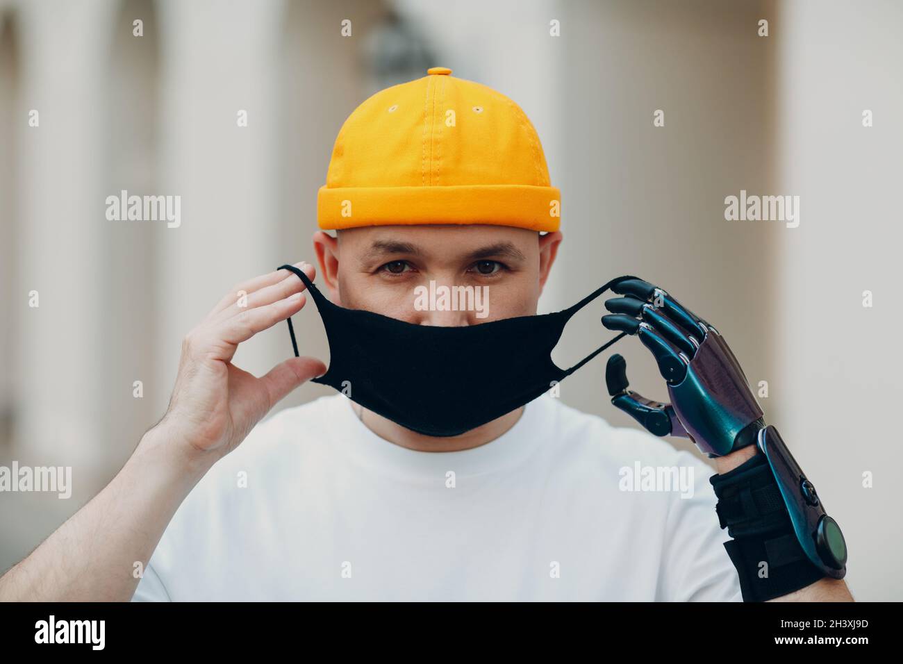 Young disabled man put on medical protective face mask with artificial prosthetic hand. Stock Photo