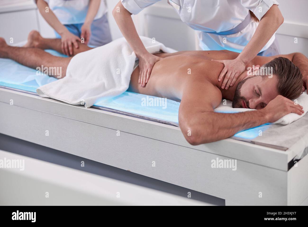 Professional chiropractics do massage of back and leg to mature man lying on couch in hospital Stock Photo