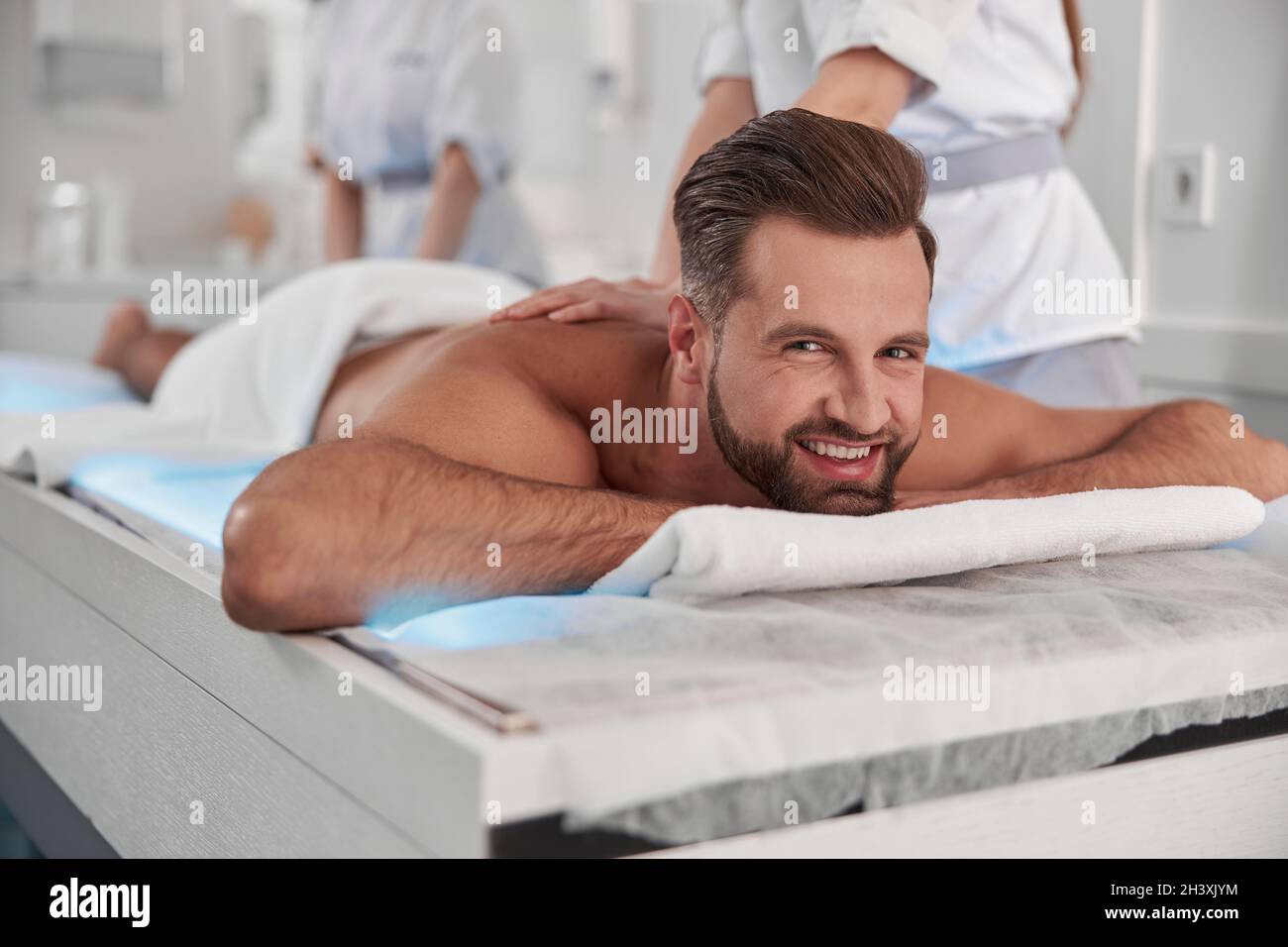 Happy mature man undergoes massage procedure with professional chiropractics in clinic Stock Photo